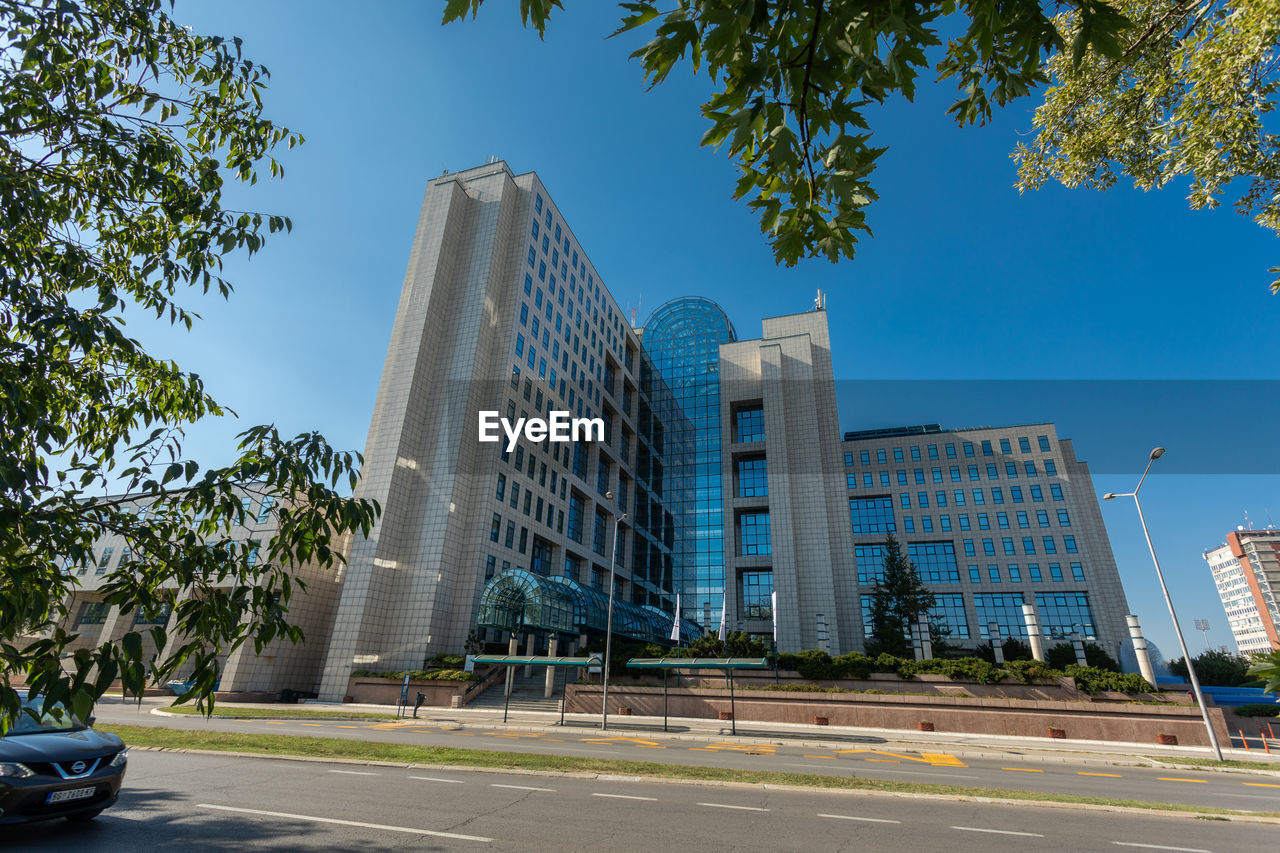 architecture, city, built structure, building exterior, metropolitan area, office building exterior, downtown, building, tree, transportation, neighbourhood, road, skyscraper, urban area, sky, street, landmark, tower block, office, car, plant, residential area, nature, motor vehicle, travel destinations, city street, travel, metropolis, mode of transportation, blue, downtown district, cityscape, day, city life, residential district, outdoors, landscape, no people, plaza, business, urban skyline, clear sky, business finance and industry, construction industry, sign, finance, symbol, vehicle, condominium