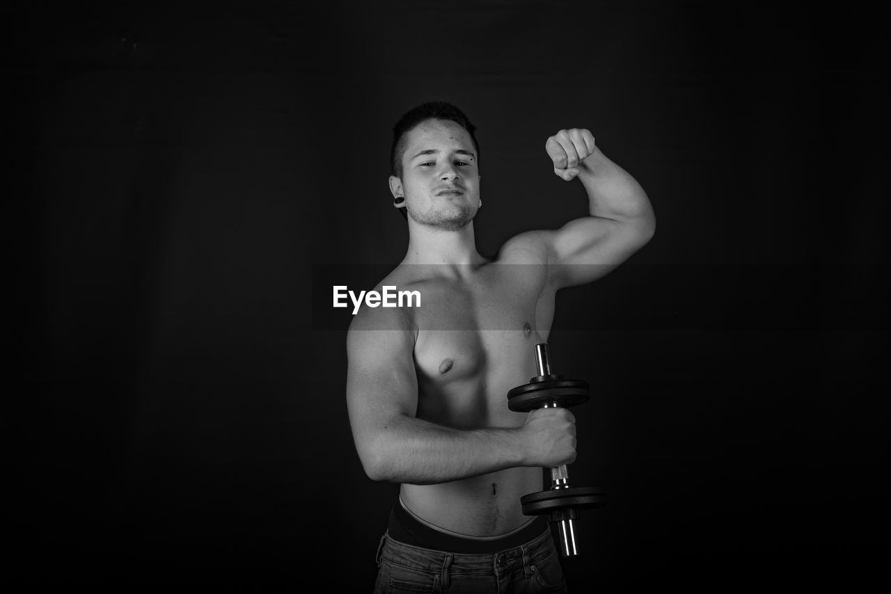 Portrait of shirtless man lifting dumbbells against black background