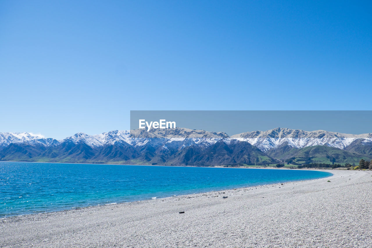 Scenic view of sea and mountains against clear blue sky