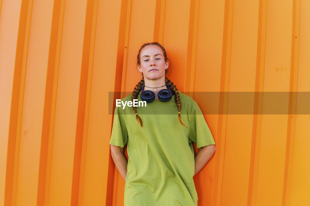 Young woman with hands behind back standing in front of orange wall