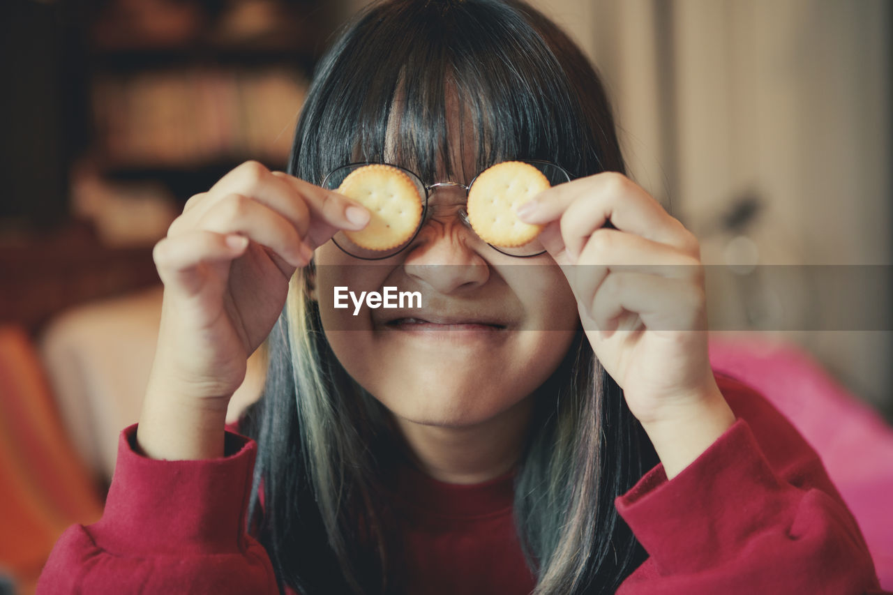 Close-up of smiling girl holding snack against face