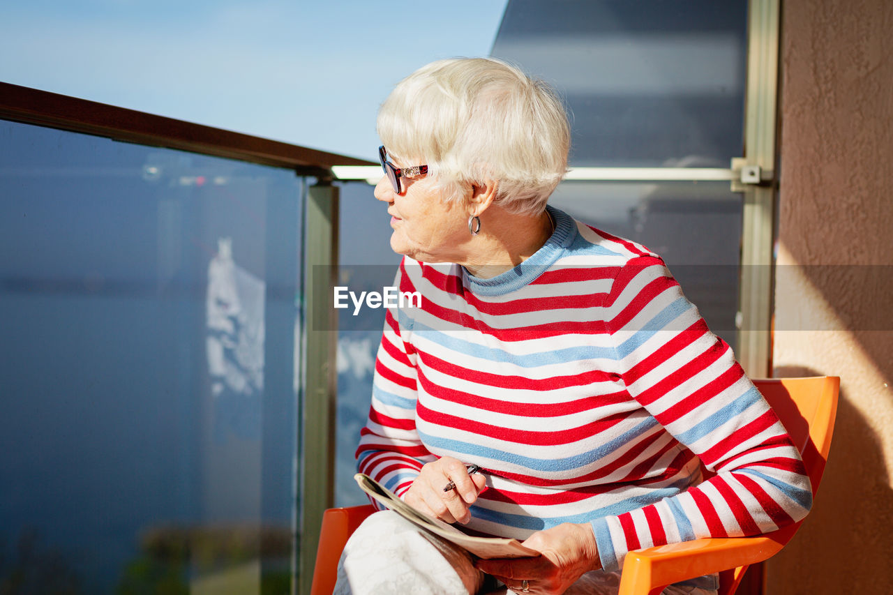 Senior woman in glasses sitting on balcony near the sea