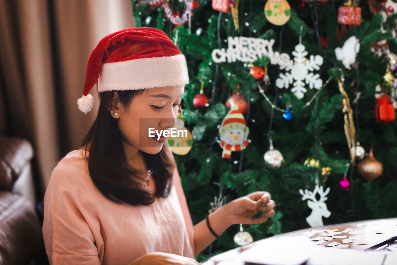 Beautiful woman in red santa hat sitting near the christmas tree