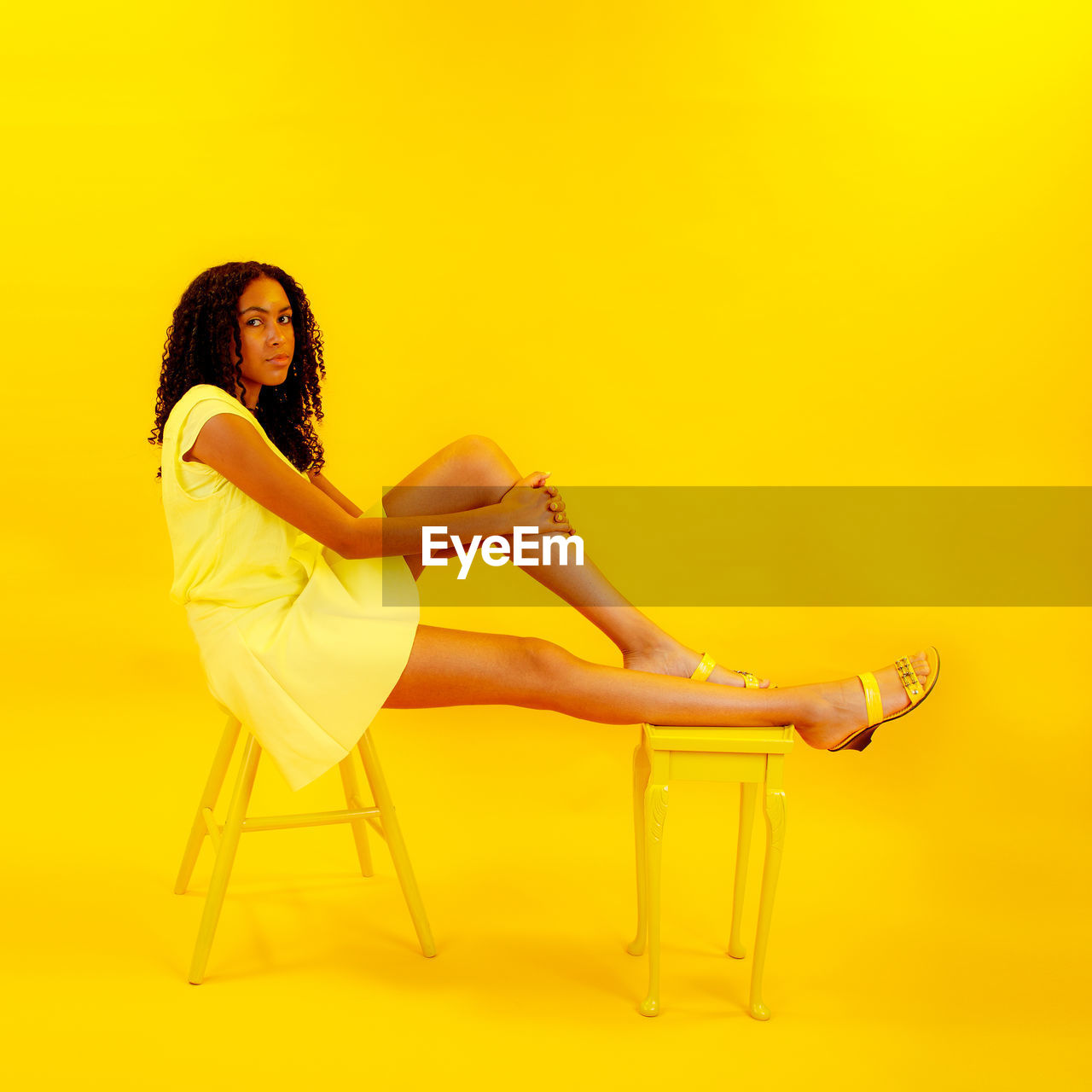 Side view portrait of teenage girl sitting on stools against yellow background