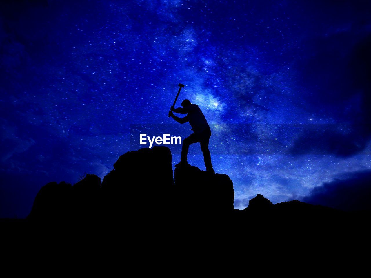 Silhouette man hammering rock against star field at night