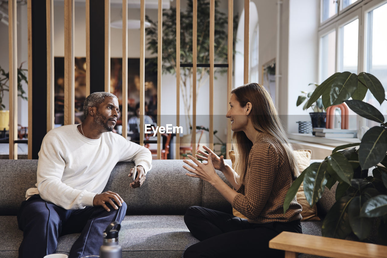 Businesswoman discussing with male colleague while sitting on sofa at coworking office