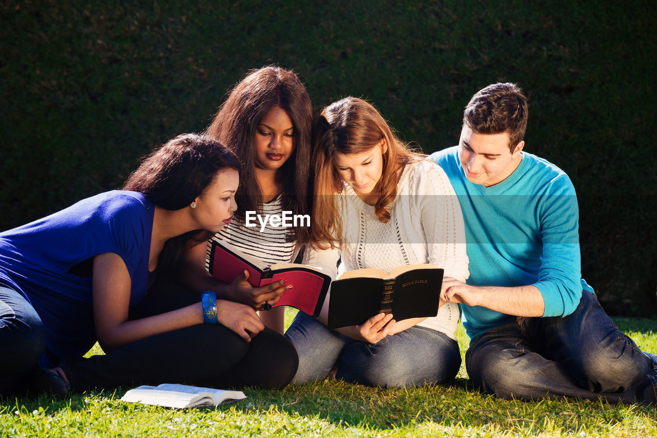 Friends reading bible while sitting on field