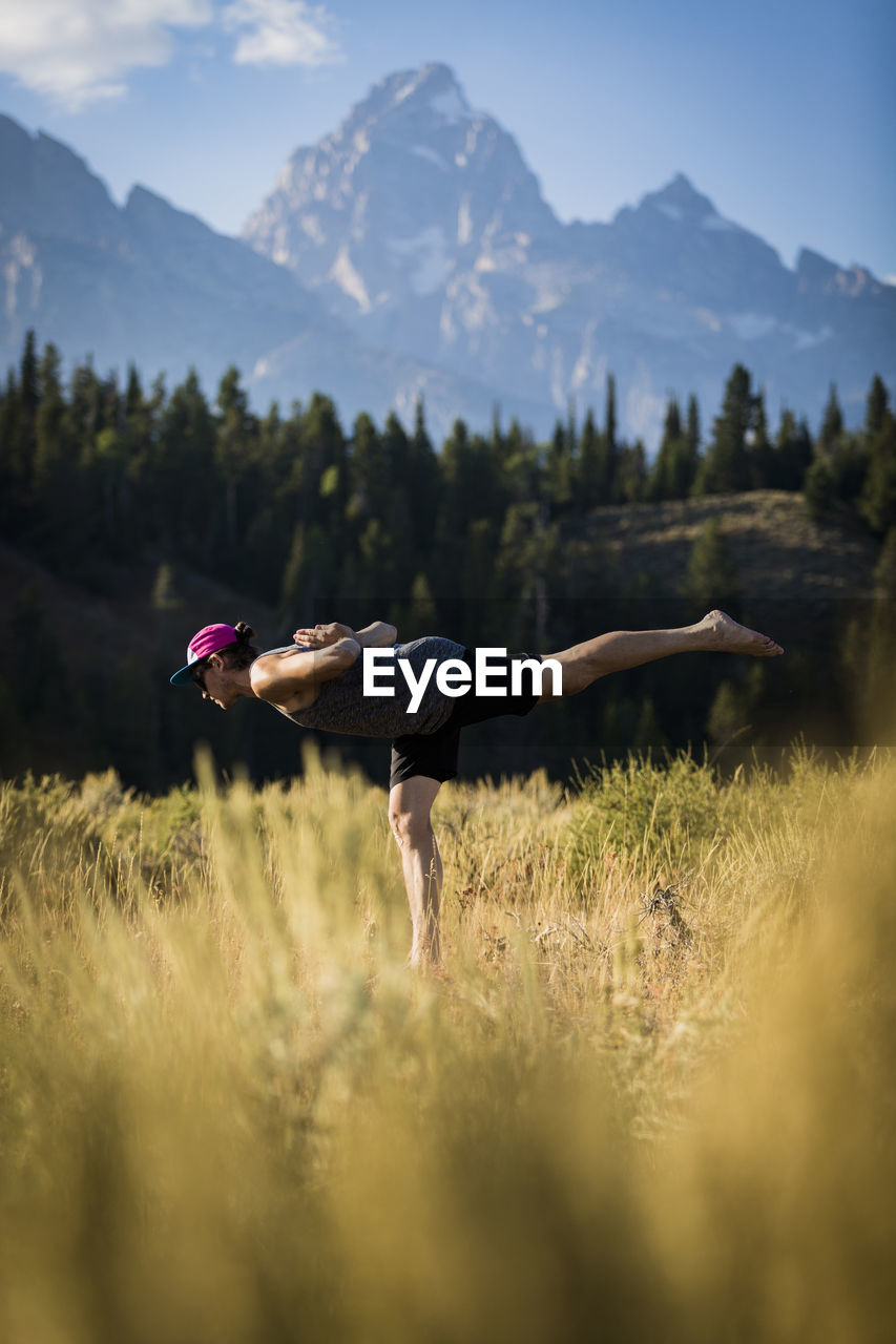 Side view of man standing on one leg while practicing yoga on field at bridger-teton national forest