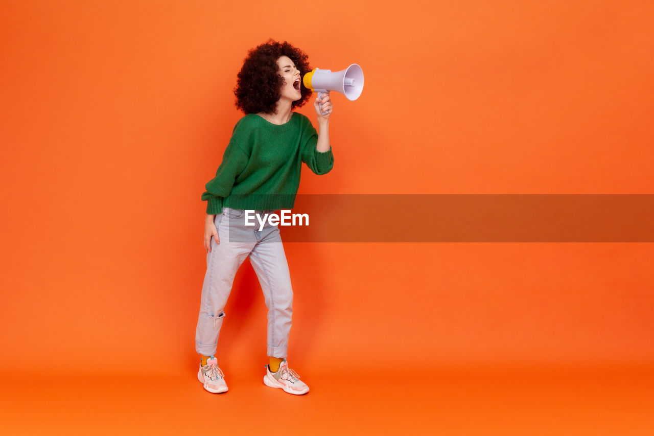 full length of young woman with arms raised against yellow background