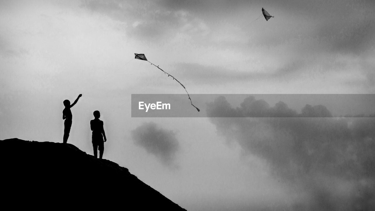 Low angle view of silhouette boys flying against sky