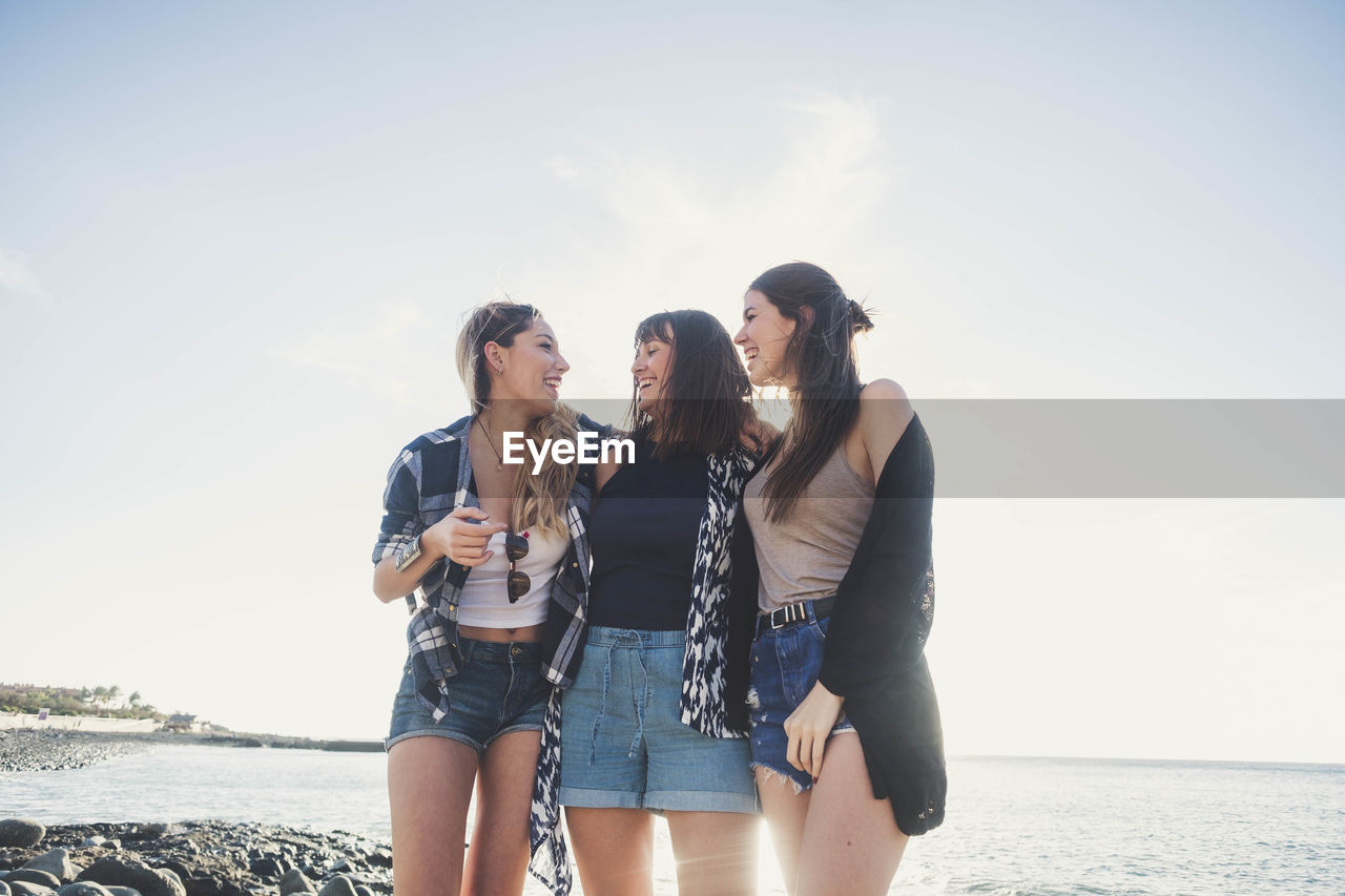 Friends standing at beach against sky