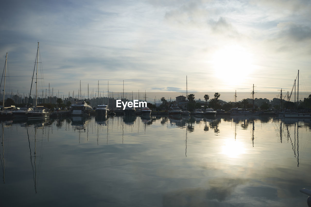 SAILBOATS MOORED AT HARBOR DURING SUNSET