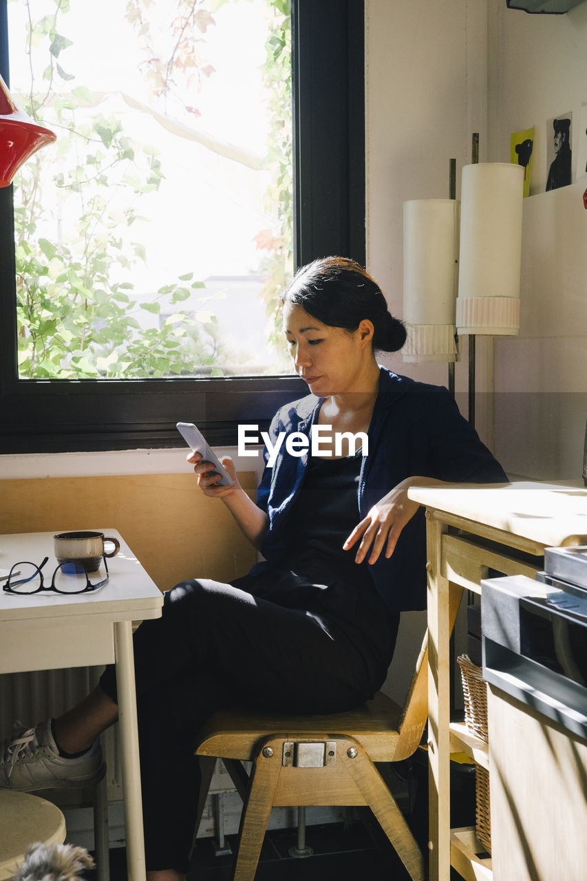 Female architect using smart phone while sitting at desk in home office