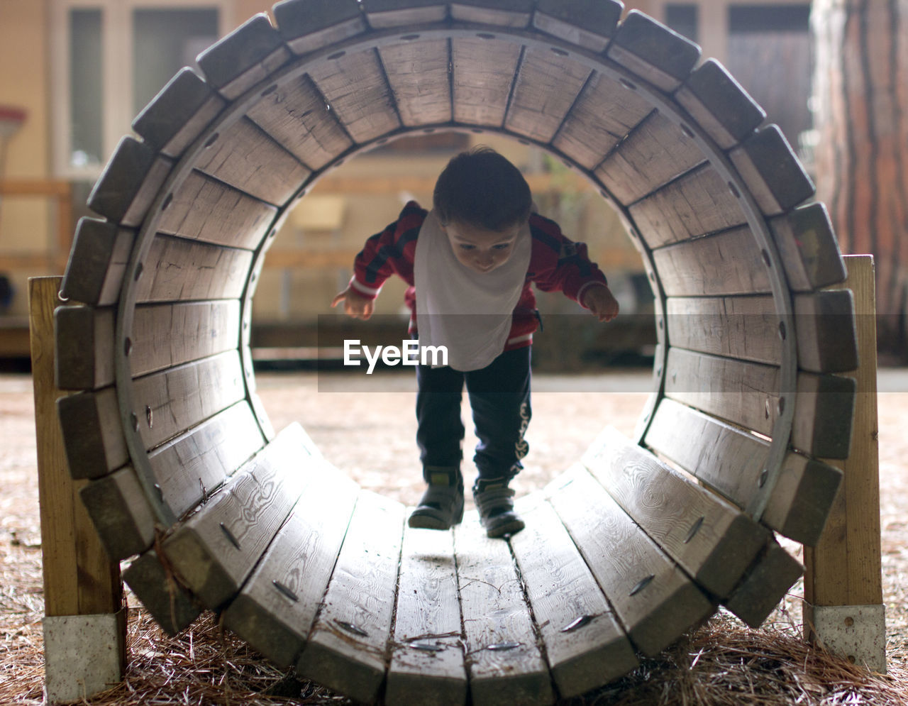 Full length of boy walking through wooden pipe at playground