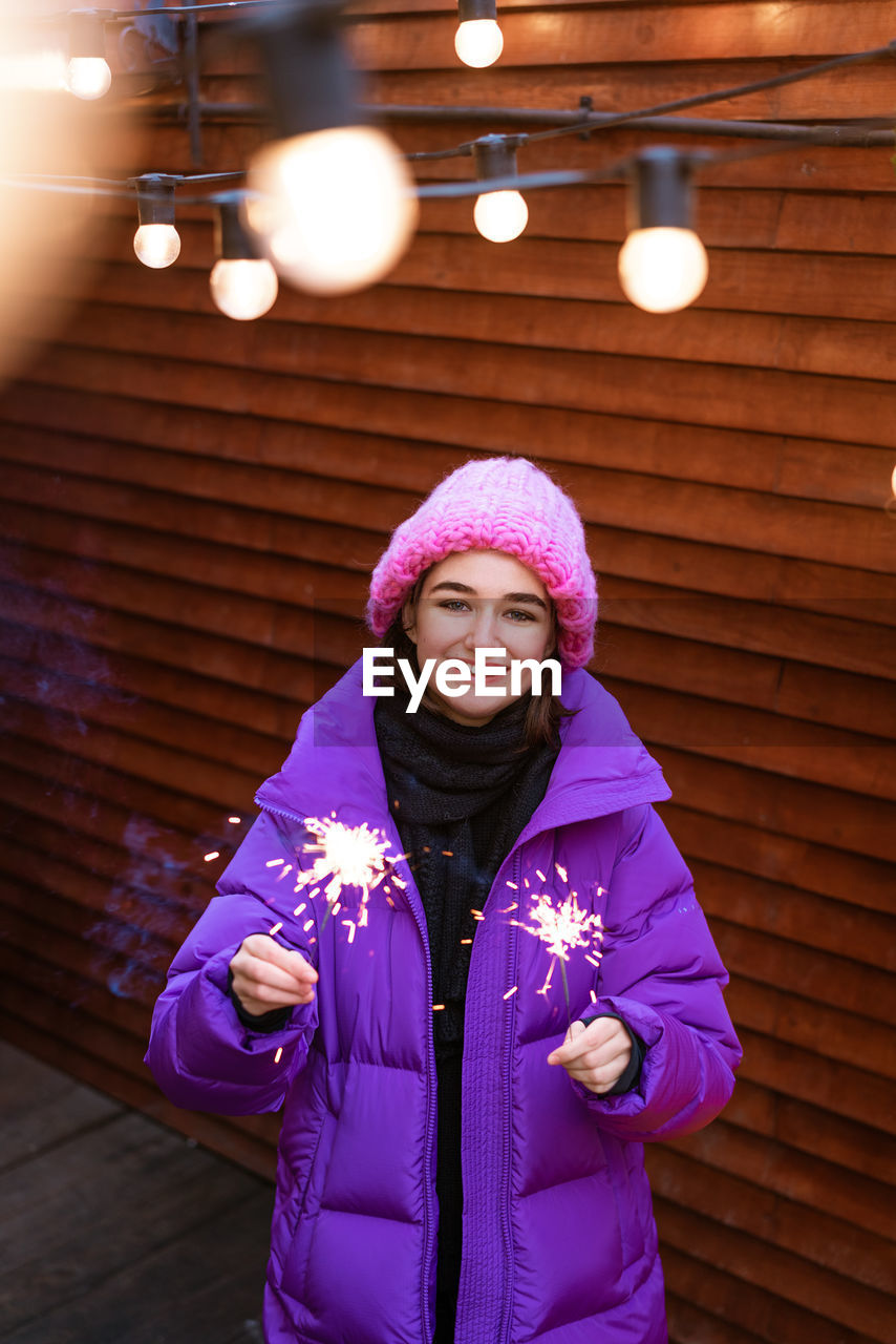 Happy young woman in outerwear with sparklers on the street on the background