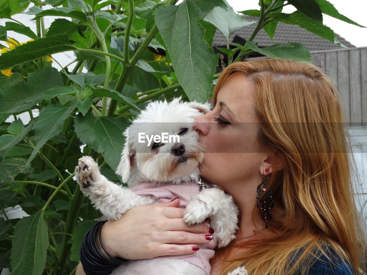 Young woman with long hair kissing dog by leaves