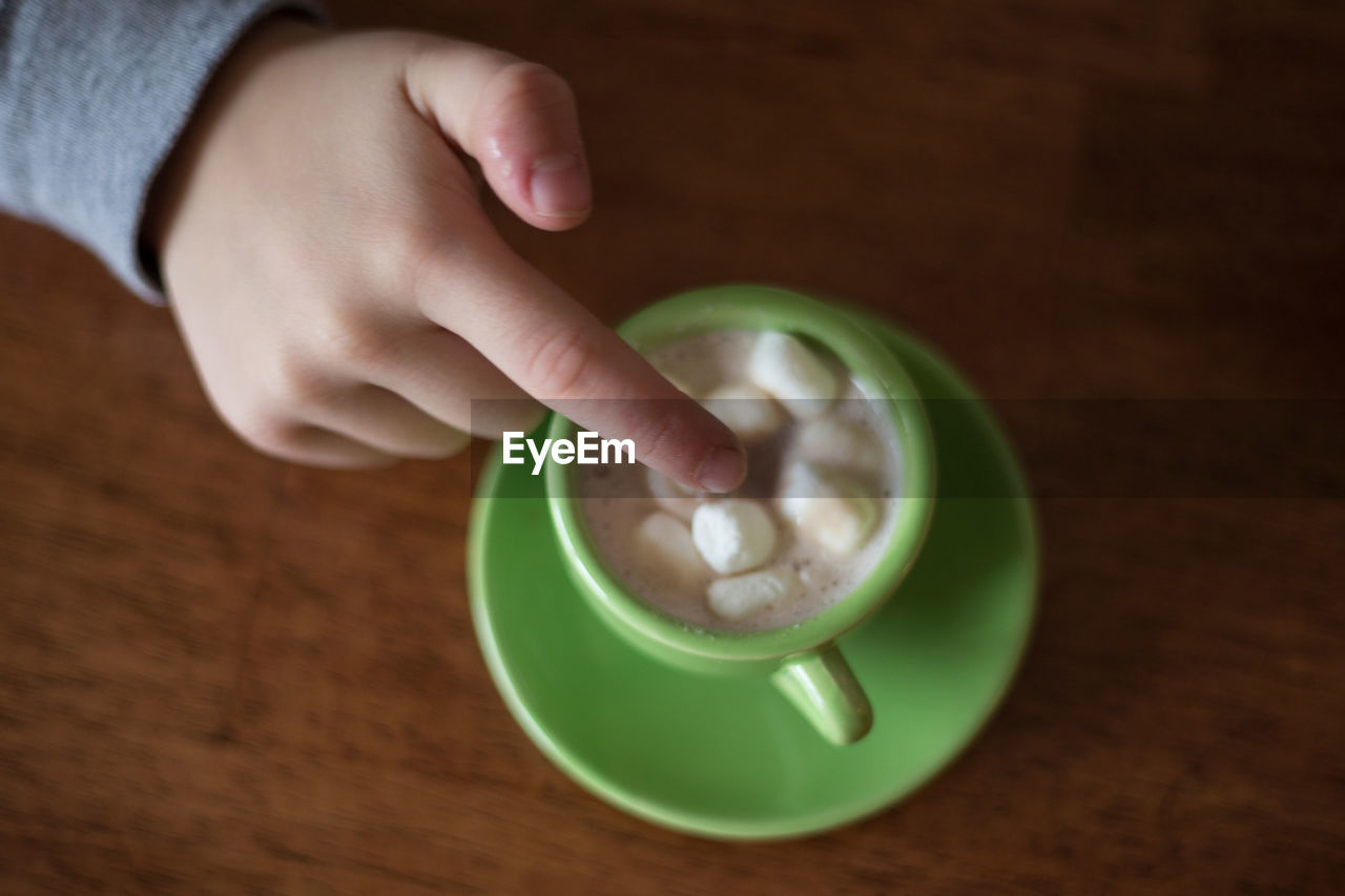 Cropped hand touching sugar cubes in cup at table