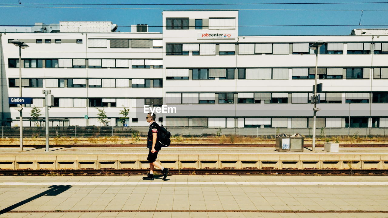 SIDE VIEW OF MAN ON RAILROAD TRACK AGAINST BUILDINGS