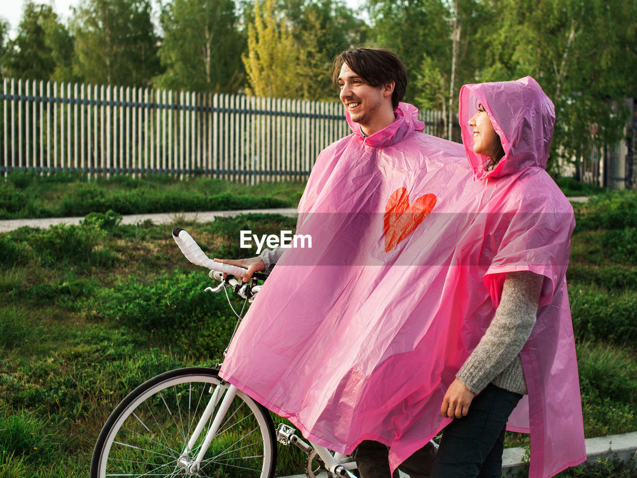 Couple with bicycle wearing pink raincoat