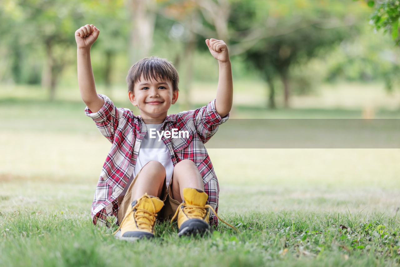 PORTRAIT OF SMILING BOY WITH ARMS RAISED