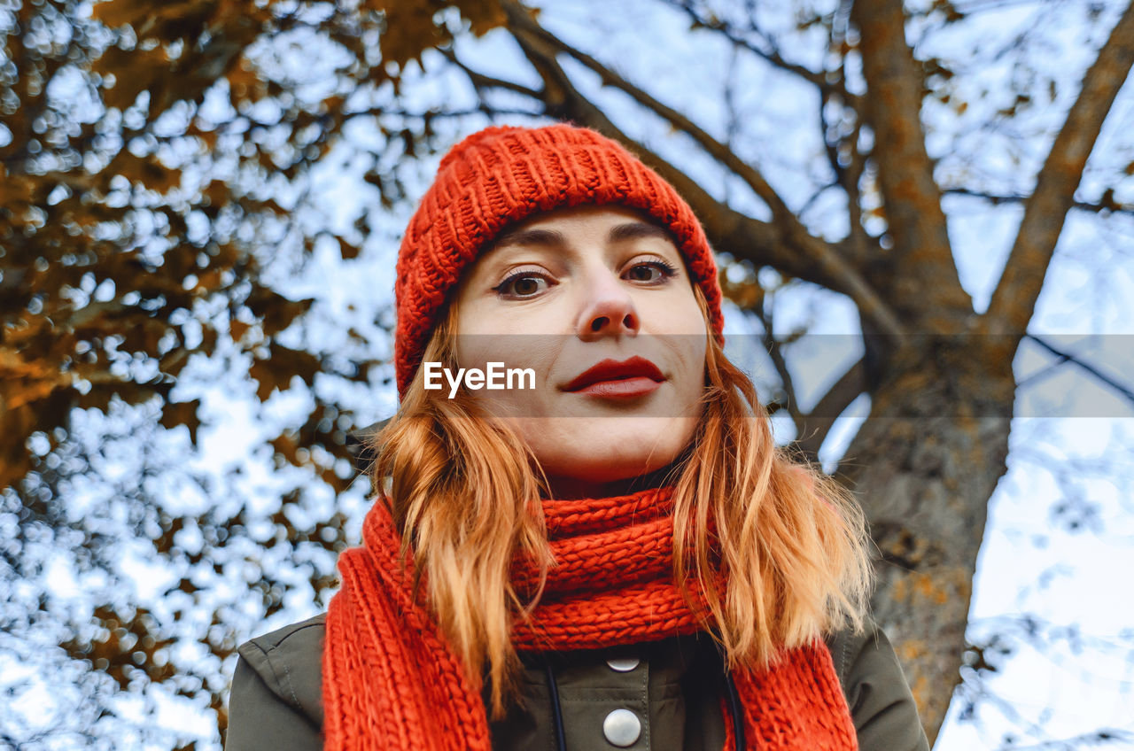 Bright cute young woman in orange warm knitted hat and scarf. autumn portrait close-up.