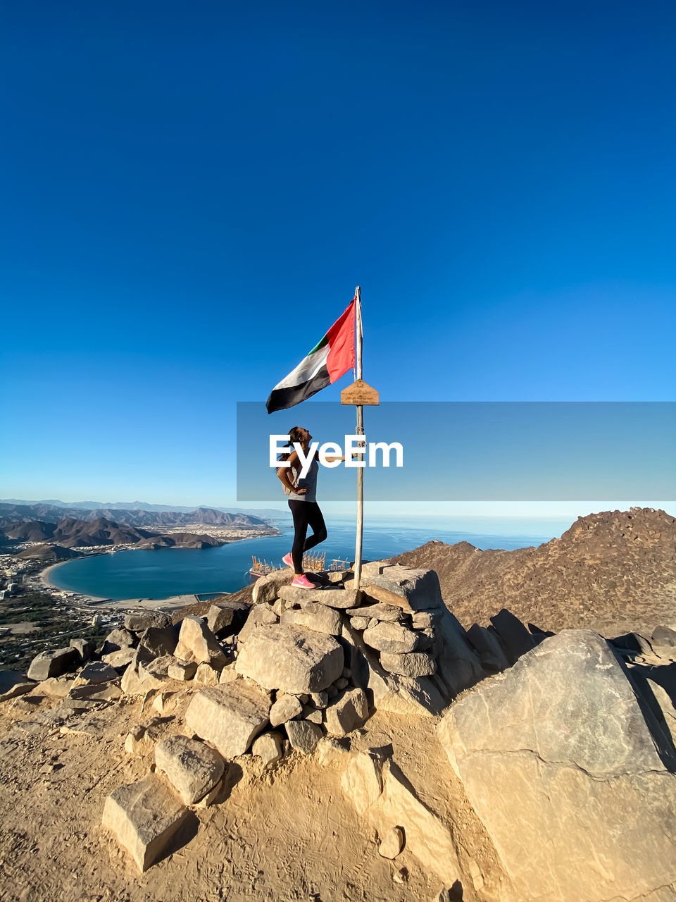 MAN STANDING ON ROCK AGAINST BLUE SKY