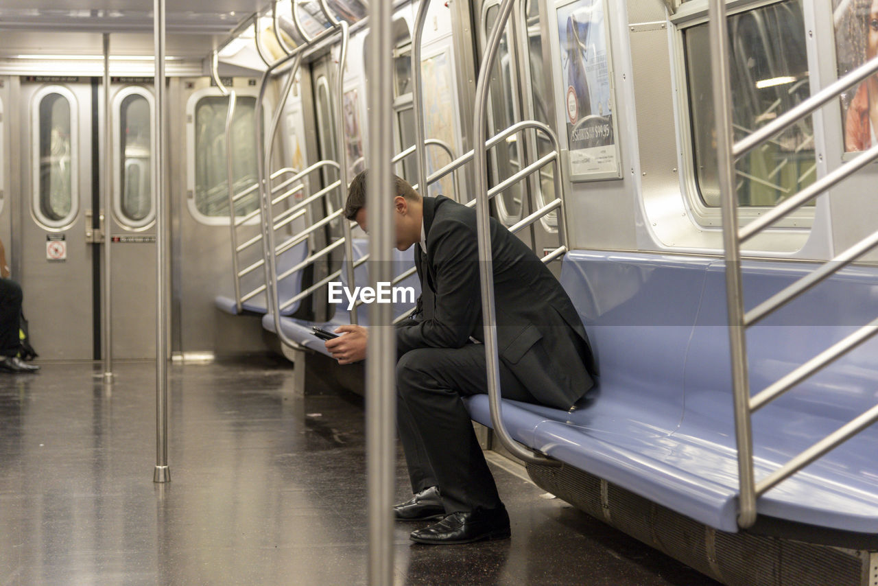 Businessman alone on a subway car, sitting and scrolling through his smart phone device.