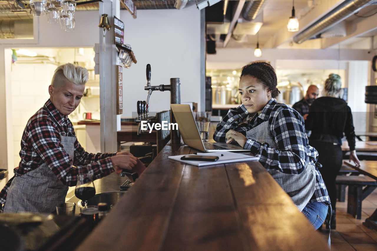 Woman using laptop while standing by partner at bar counter