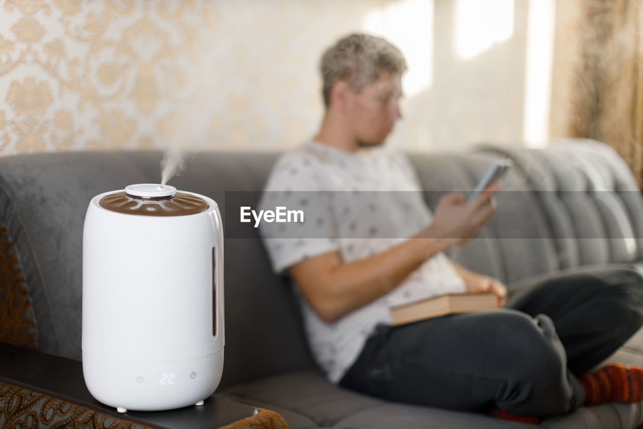 Air humidifier stay in living room. selective focus on vapor. on blurred background caucasian man