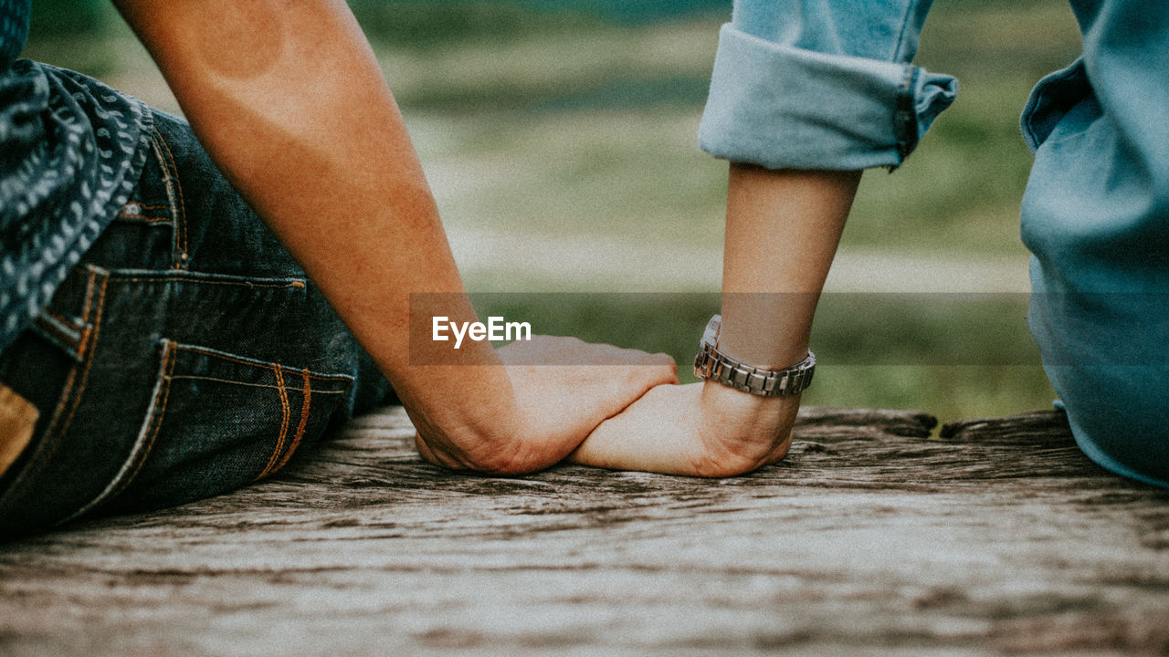 Cropped image of couple holding hands while sitting on bench