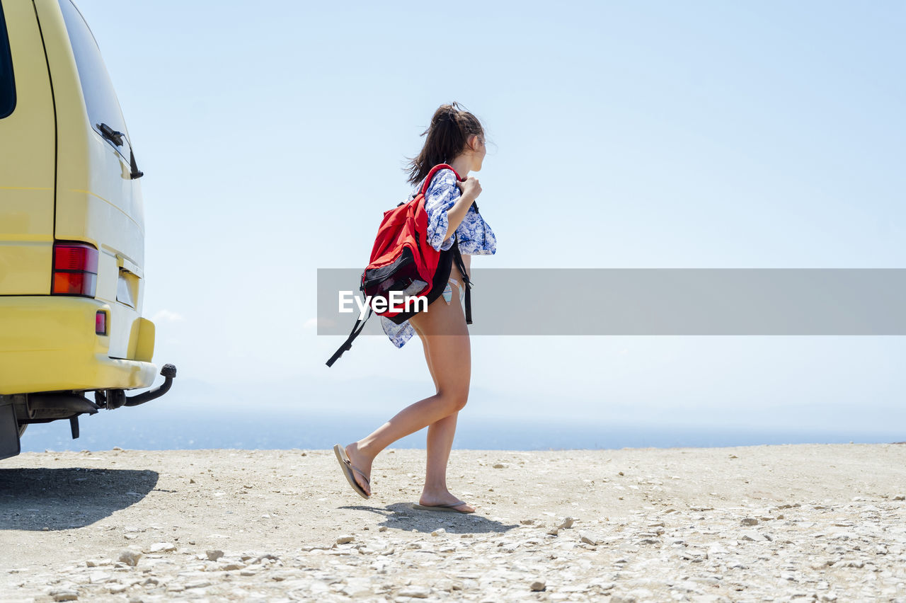 Mid adult woman carrying backpack while walking at beach during summer