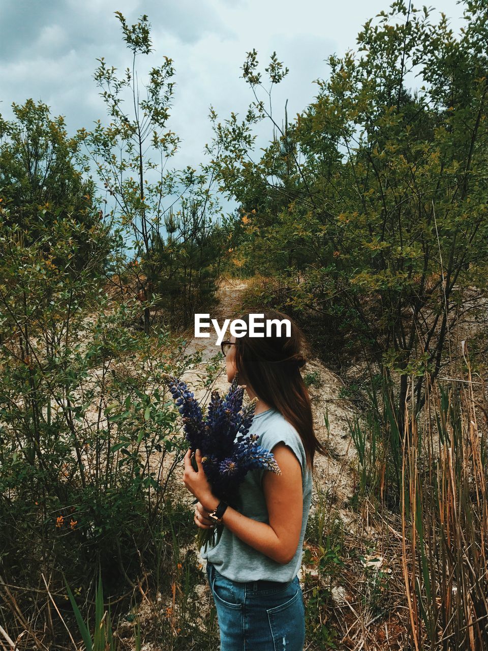 Woman holding flower bouquet while standing at field amidst plants