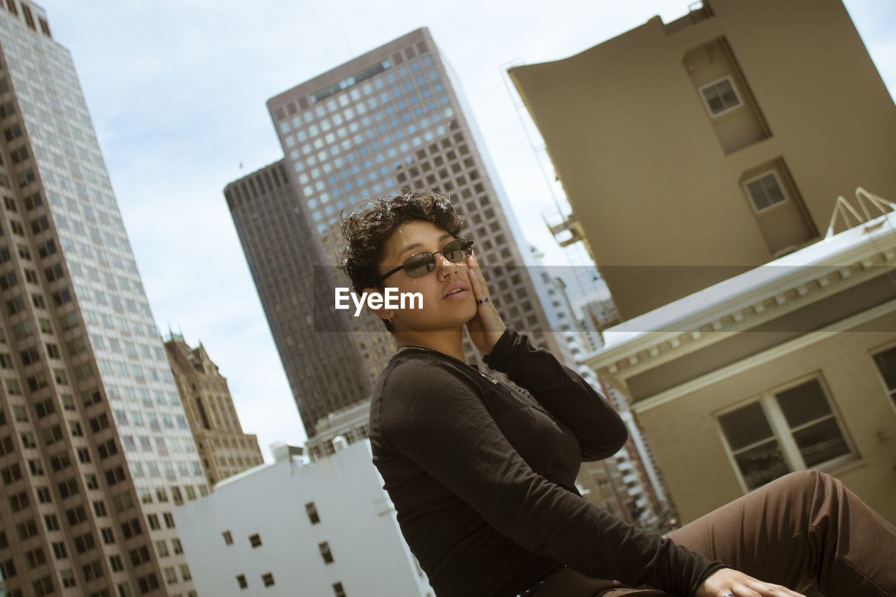 LOW ANGLE VIEW OF YOUNG WOMAN LOOKING AT BUILDINGS