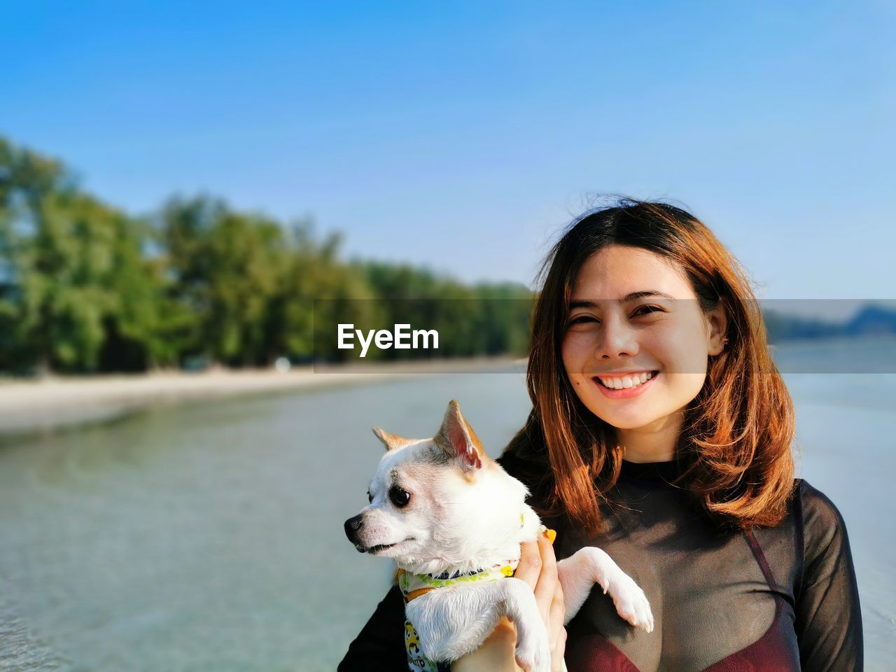 Portrait of smiling young woman holding dog against sea
