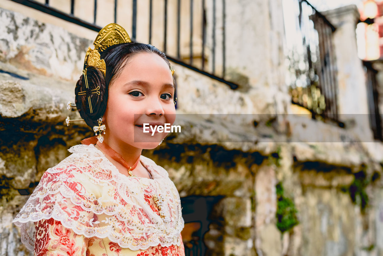 Portrait of smiling girl in pink dress standing against wall