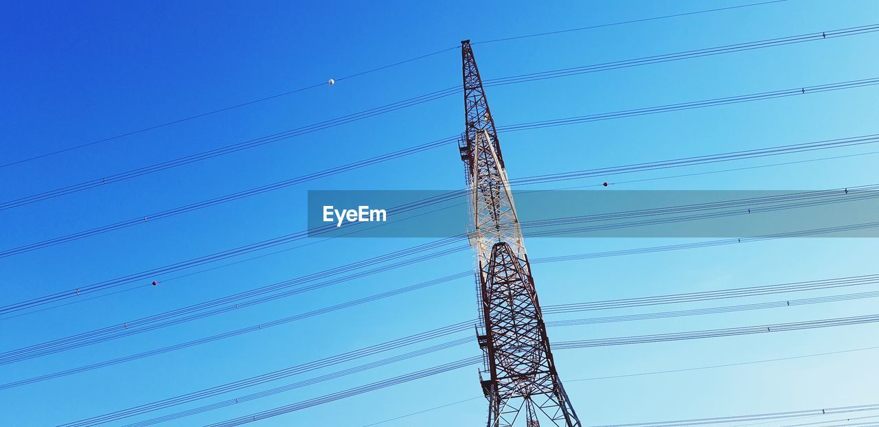 Low angle view of electricity pylon against clear blue sky