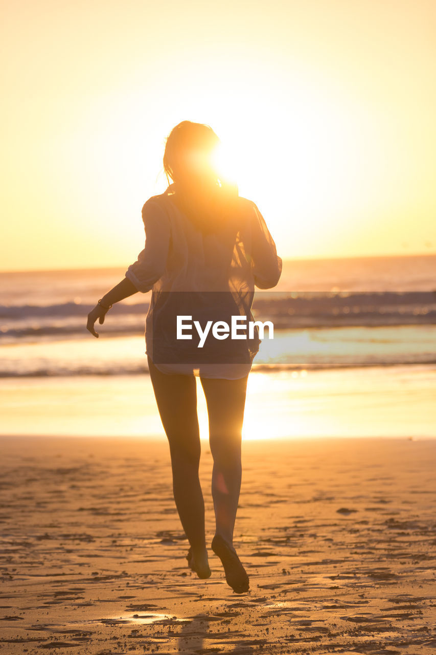 Rear view of woman running on beach during sunset