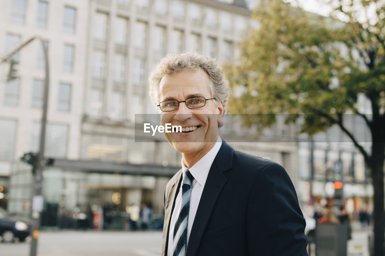 Portrait of smiling businessman wearing suit while standing in city