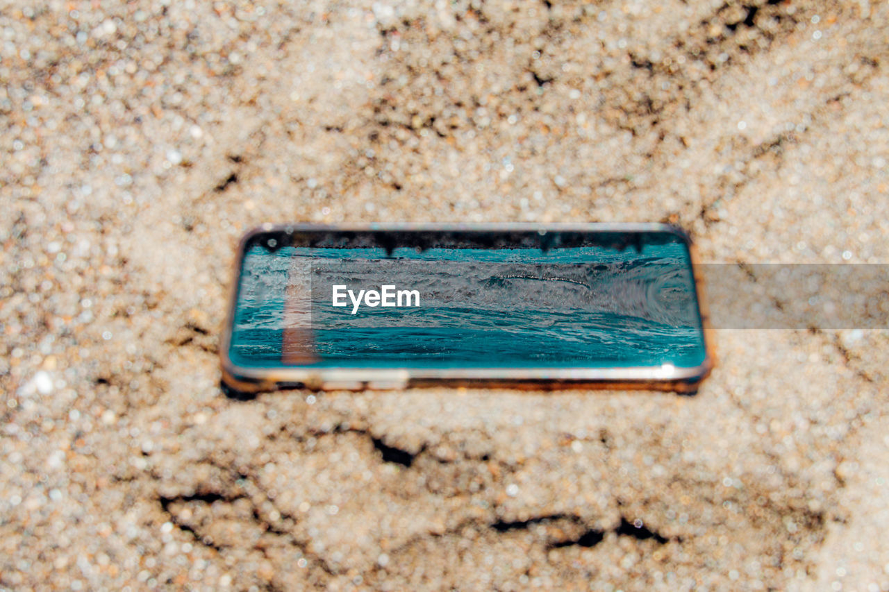 High angle view of smartphone reflected sea on the beach