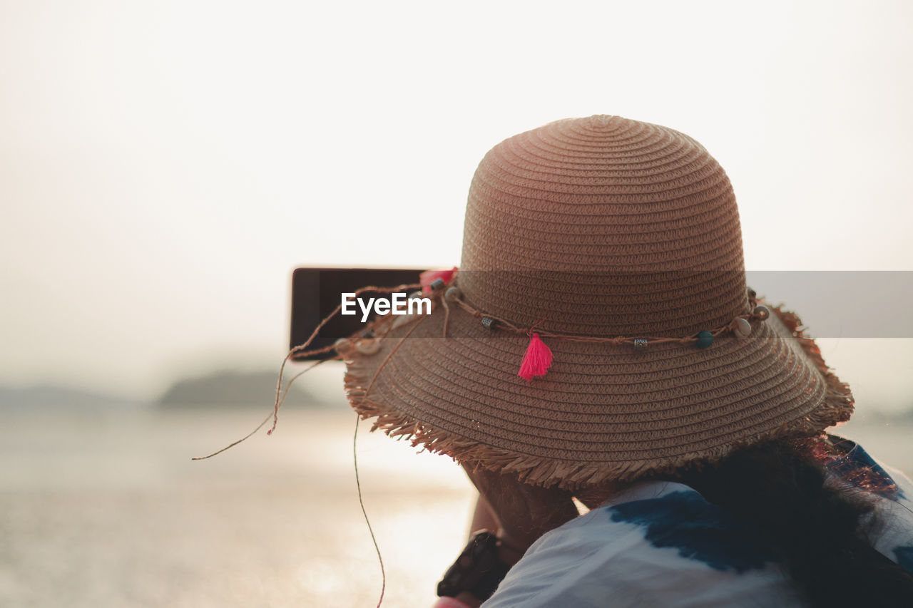 REAR VIEW OF WOMAN WEARING HAT AGAINST SUN