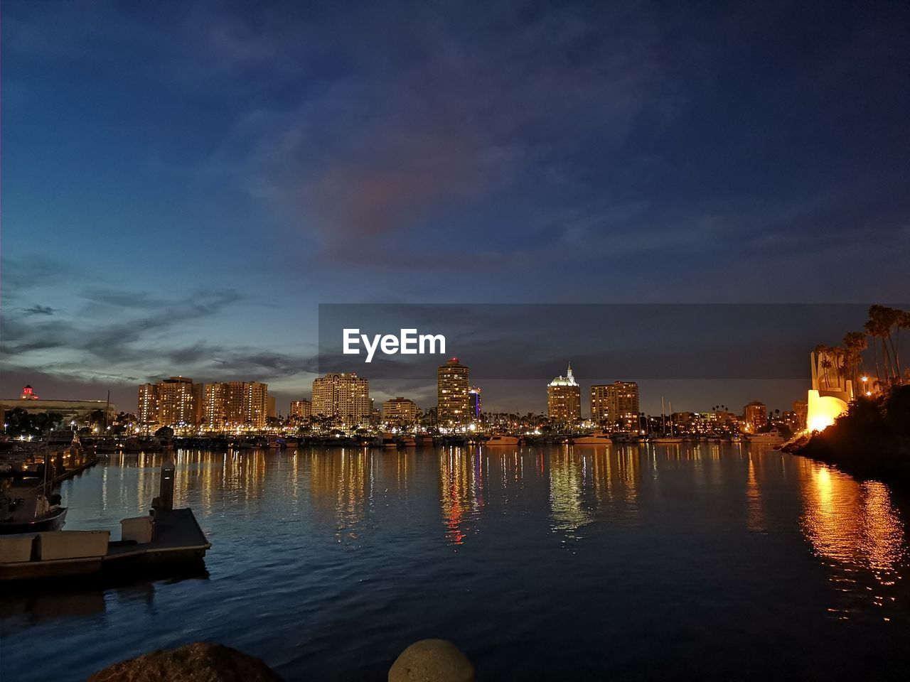 Illuminated buildings by river against sky at dusk