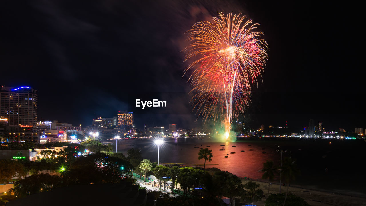 Firework display over sea against sky at night