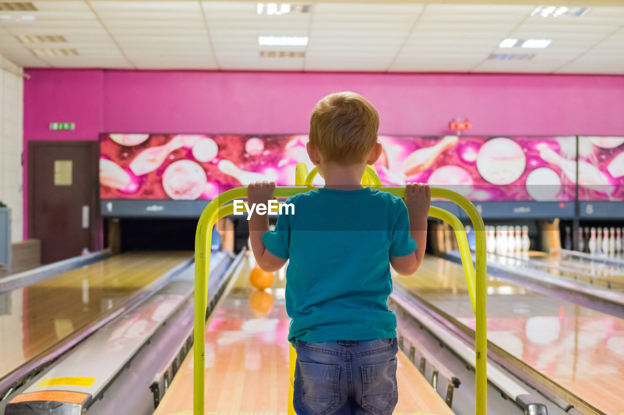 Rear view of boy standing at bowling alley