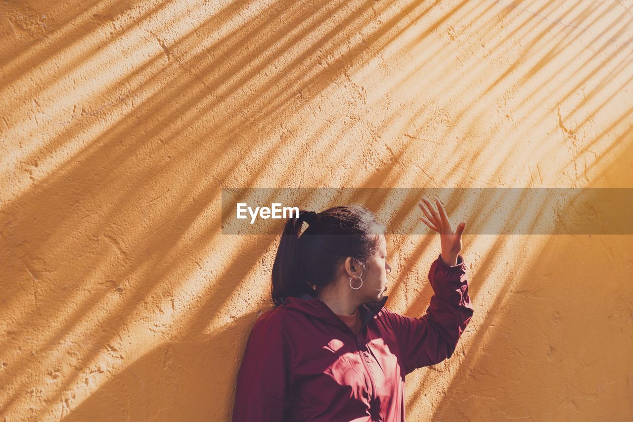 Woman gesturing standing against orange wall