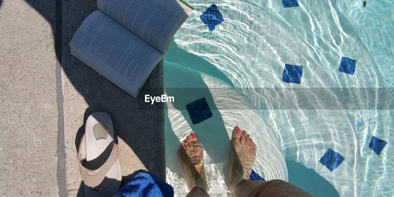 Low section of woman standing in swimming pool by book and flip-flop