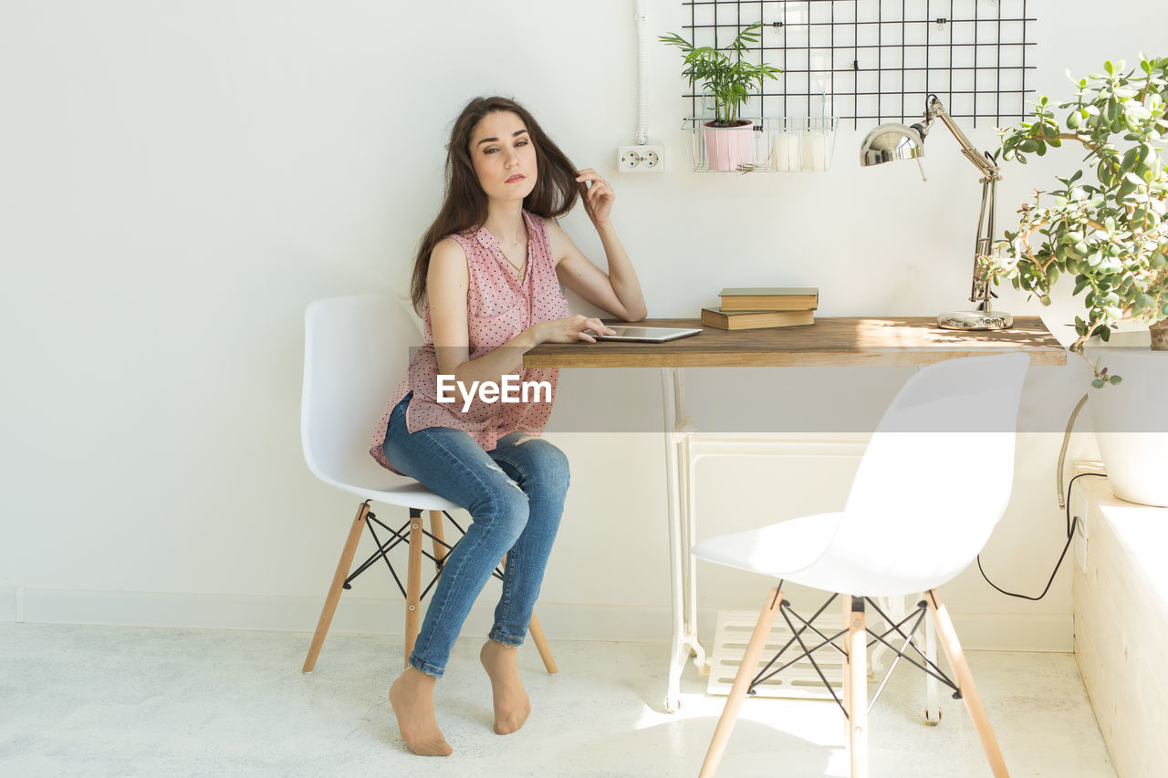 FULL LENGTH OF WOMAN SITTING ON CHAIR