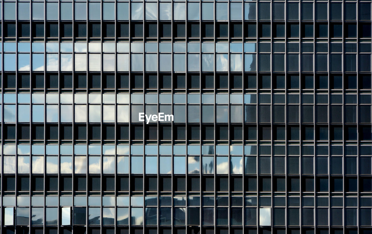 Glass curtain wall facade of a generic modern office building, with the sky reflected on its surface