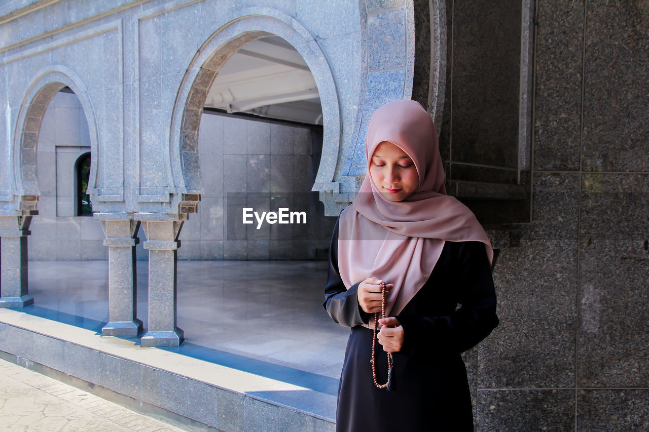 Woman in hijab holding counting rosary beads while praying at mosque