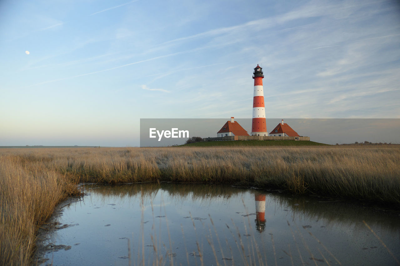 LIGHTHOUSE ON GRASS BY BUILDING AGAINST SKY