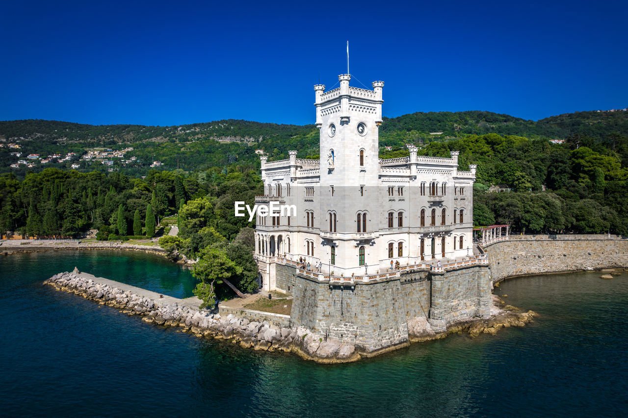 architecture, built structure, landmark, building exterior, travel destinations, château, water, nature, history, sky, travel, the past, building, blue, tower, water castle, castle, clear sky, no people, tree, tourism, plant, reflection, land, outdoors, landscape, mountain, sea, day, sunny, scenics - nature, city, environment, government, religion